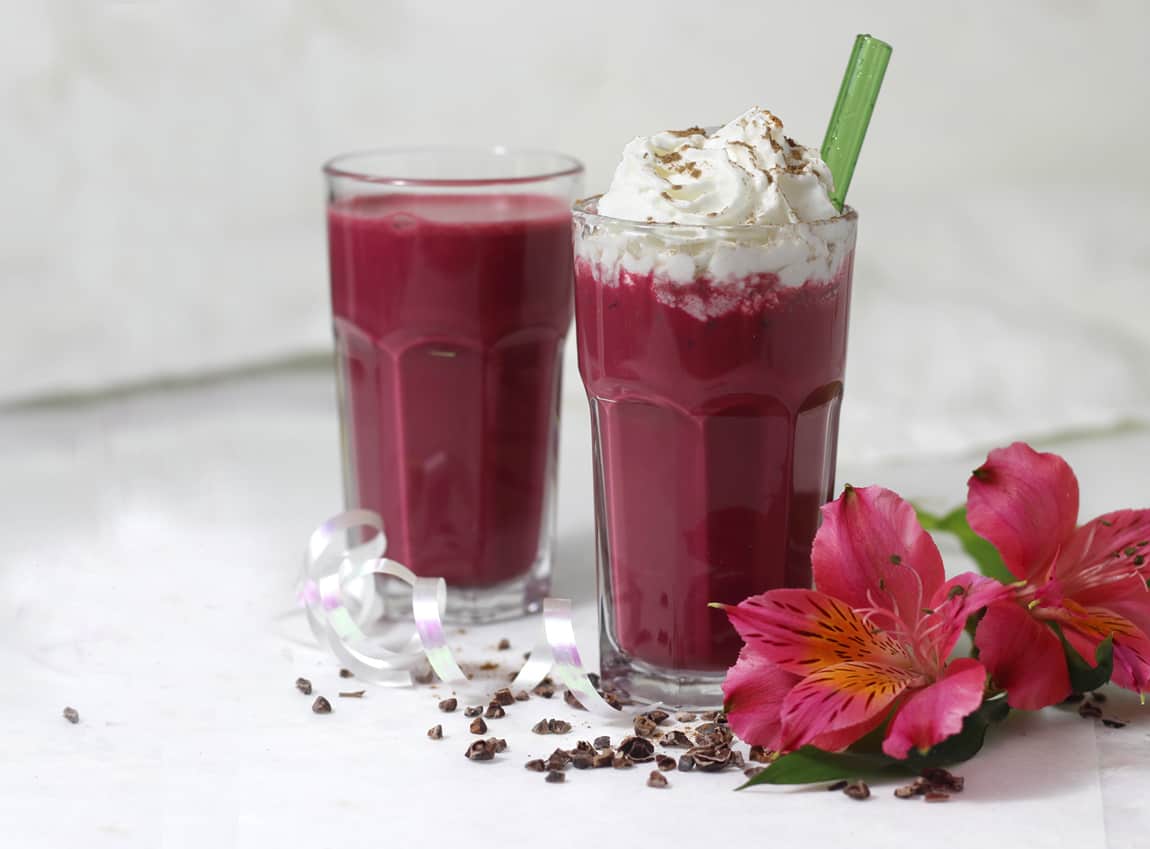 Two chocolate beet smoothies with cacao nibs scattered around.
