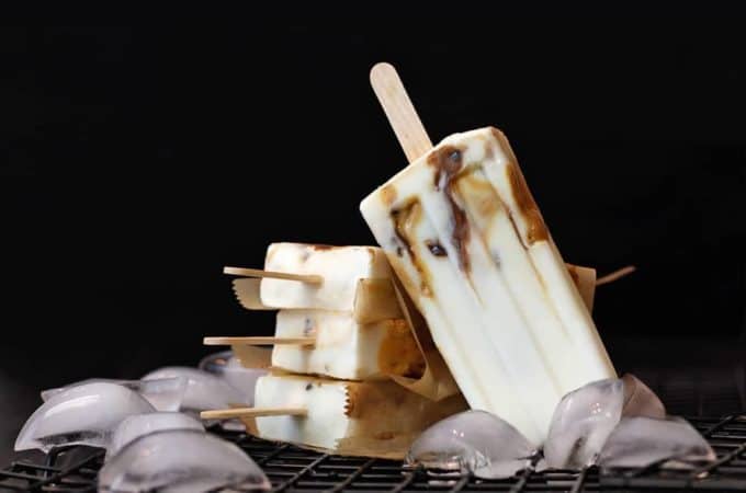 Caramel cream popsicles with date caramel and nutella ripples on ice with a black background.
