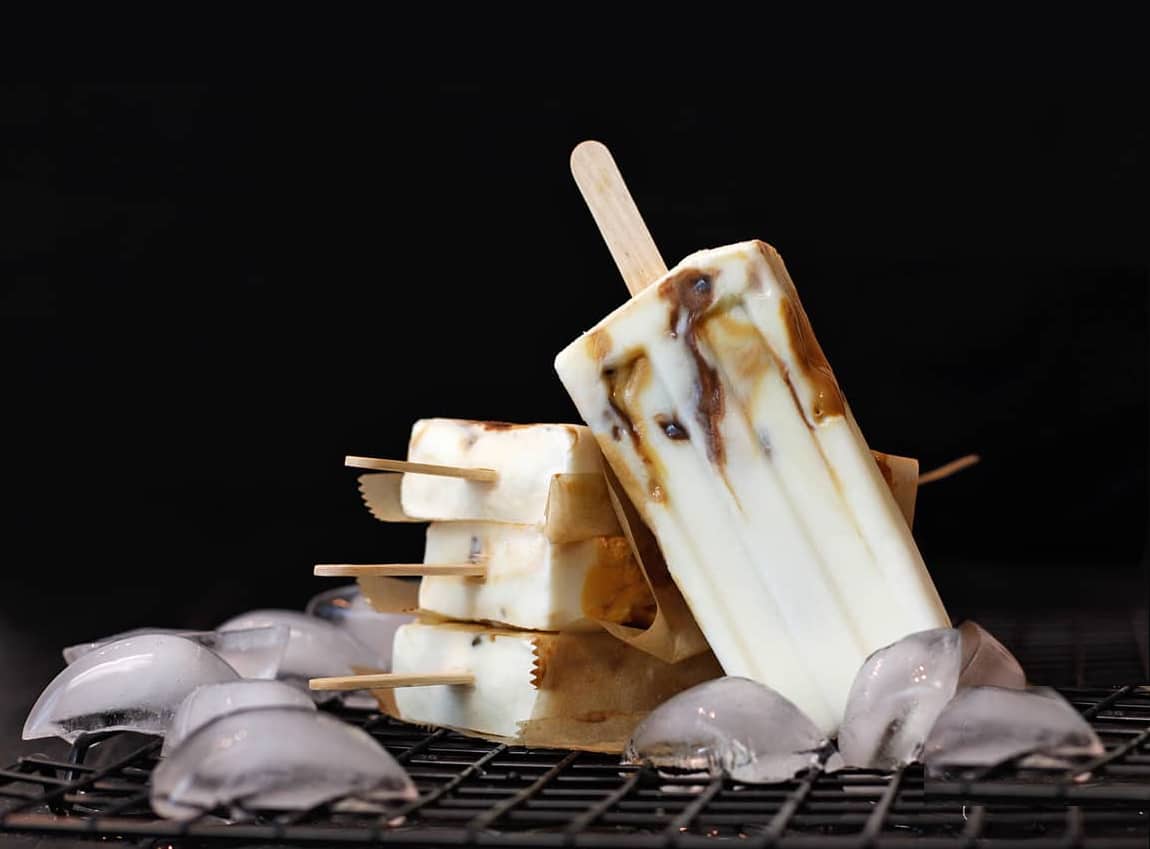 Caramel macchiato popsicles with date caramel and nutella ripples on ice with a black background.