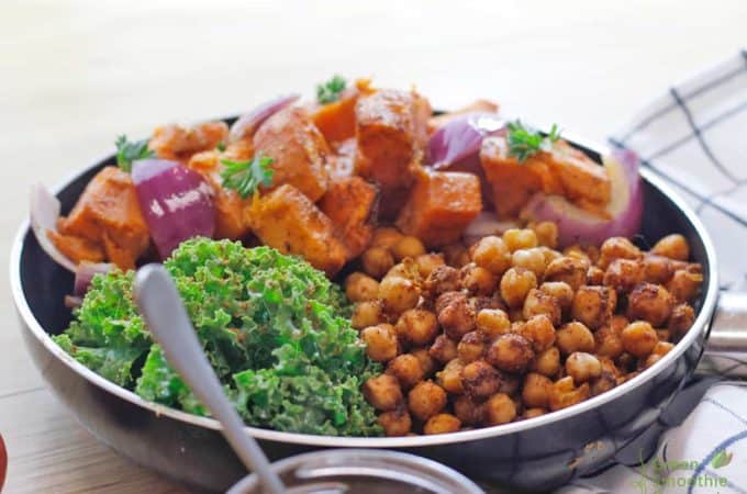A pan full of massaged kale, roasted sweet potato and chickpea tossed in tandoori spices on a table.