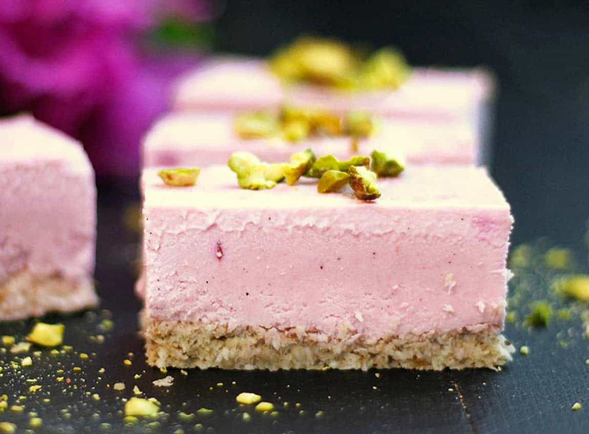 A slice of pink cheesecake on a black board.