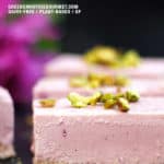 A pink vegan cheesecake recipe on a board with pink flowers behind it.