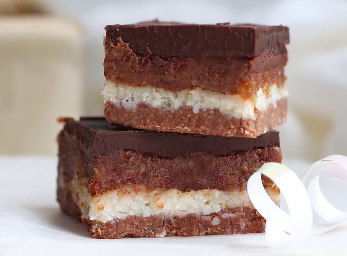 Square slices of Chocolate Caramel raw bars with a white ribbon on a white board.