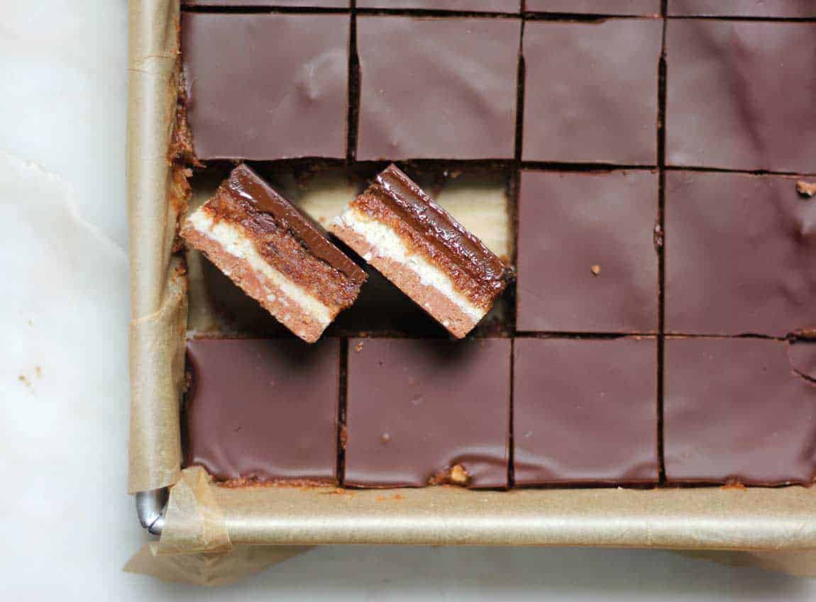 Square slices of Chocolate Caramel Cakes with a white ribbon on a white board.