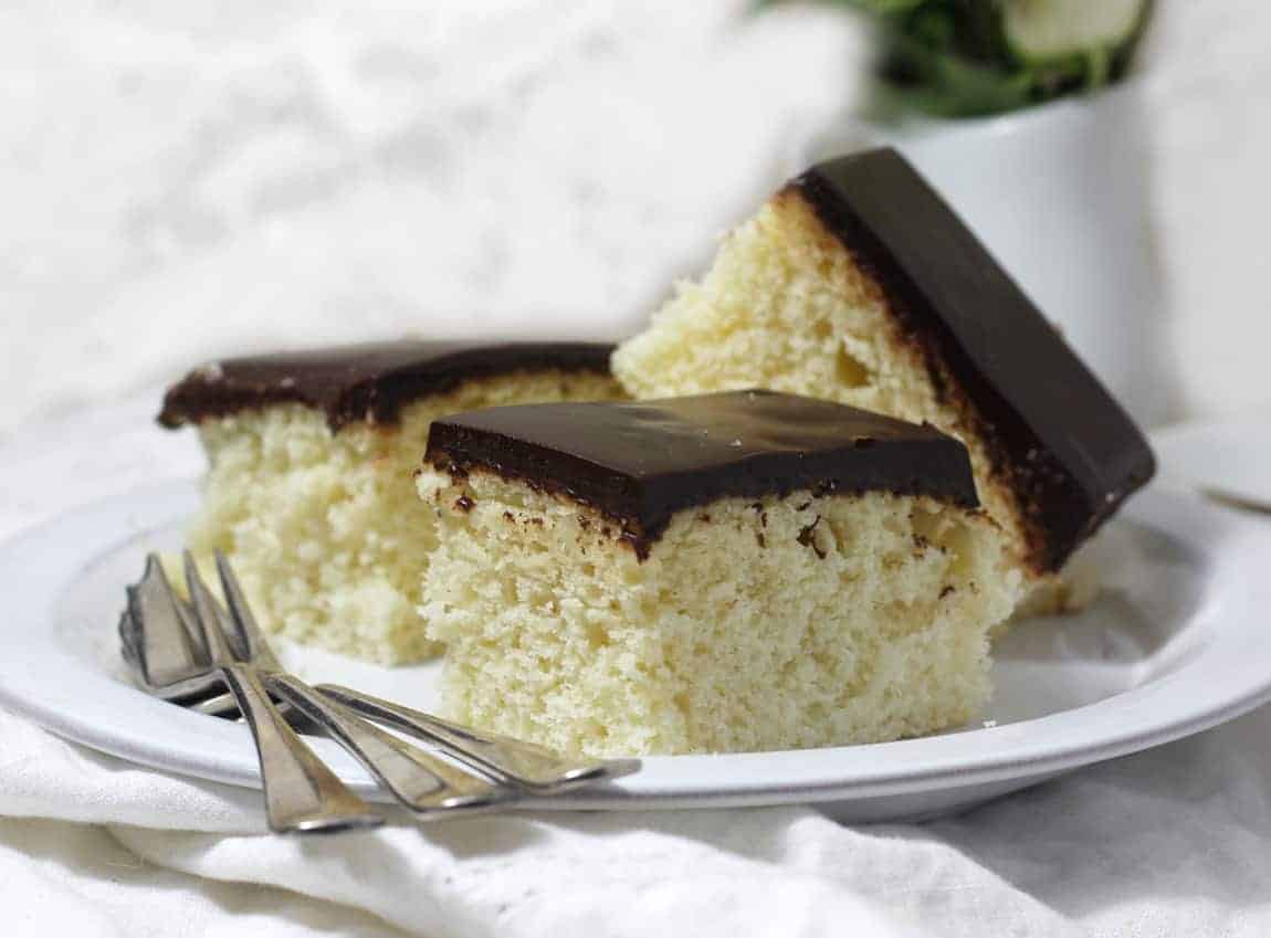 Slice of vanilla cake with chocolate icing on a white dish.