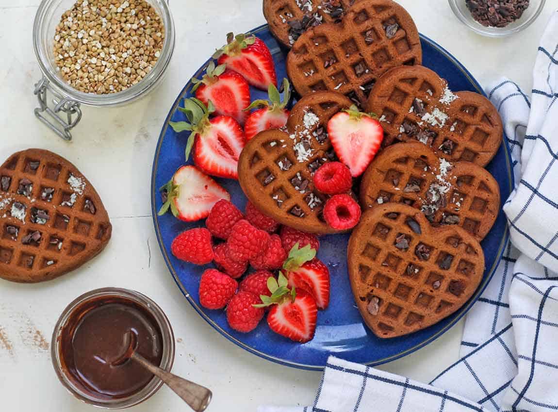 Heart buckwheat waffles on a navy dish with fruit.
