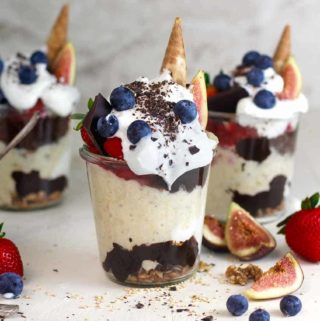 A jar with yogurt, fig smoothie, chocolate sauce and berries on top as well as upside down ice cream cones.