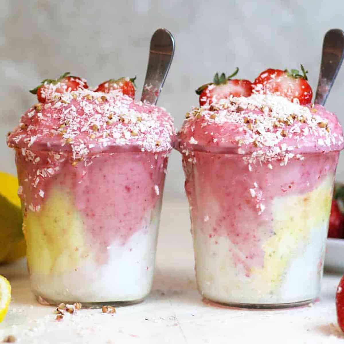 two glasses of smoothie with coconut on top and two spoons