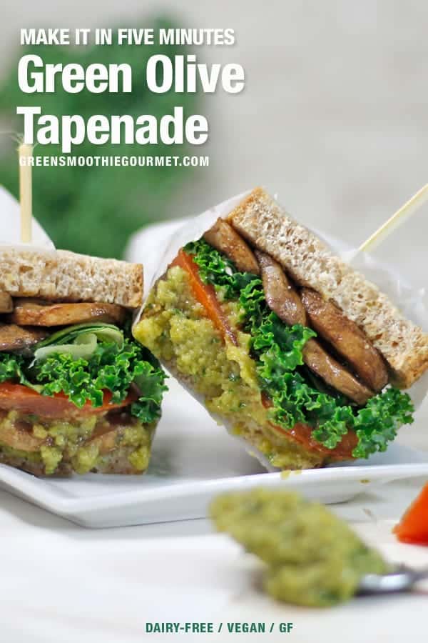 a sandwich stuffed with tomatoes, mushrooms, kale, and spilling over with green olive tapenade which is also on a spoon to the right.