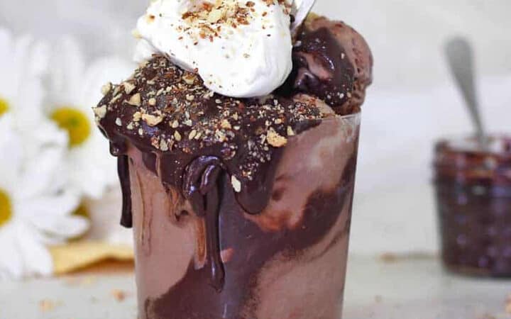 a jar of chocolate ice cream with whipped cream and chocolate syrup on top