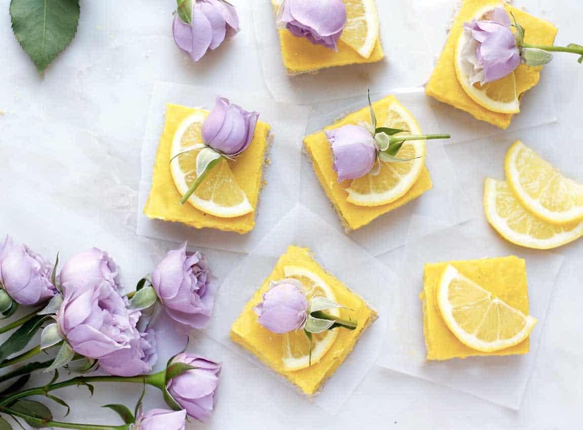 Lemon squares on a white board with purple rose on each one.