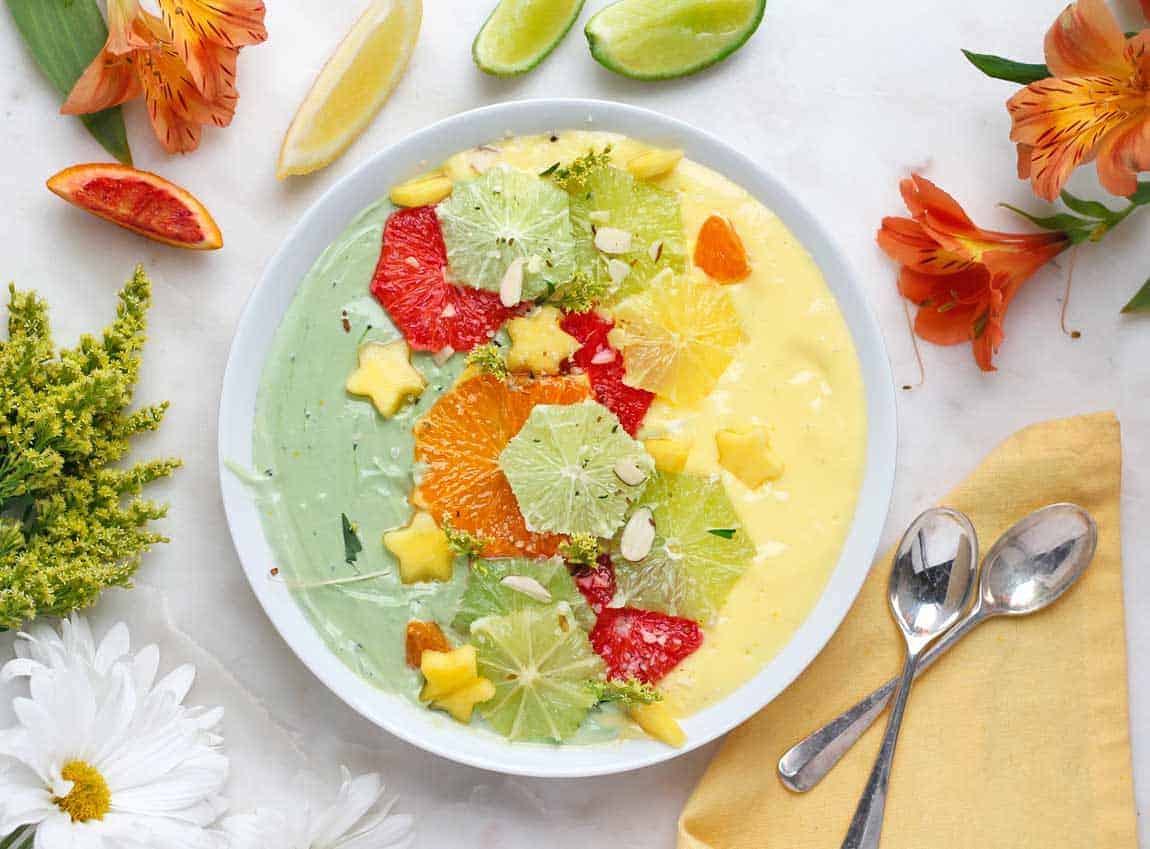 Matcha smoothie bowl with a orange jackfruit smoothie side and sliced citrus on top.