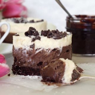 Three layered chocolate mousse cake with a chocolate pot in background.