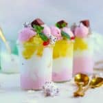 Jars of strawberry smoothie in layers in jars with gold spoons on white table.