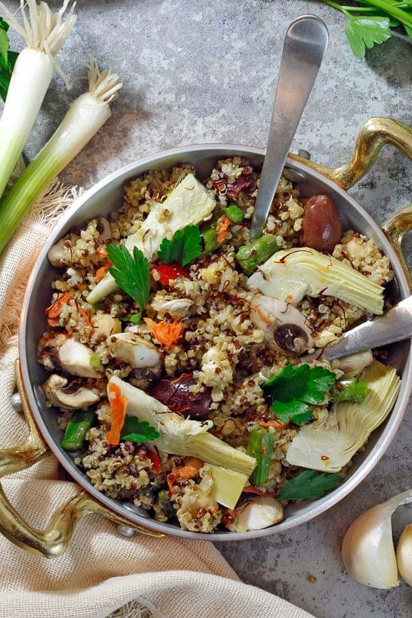 Overhead shot of quinoa in a vegan paella dish on a metal background.