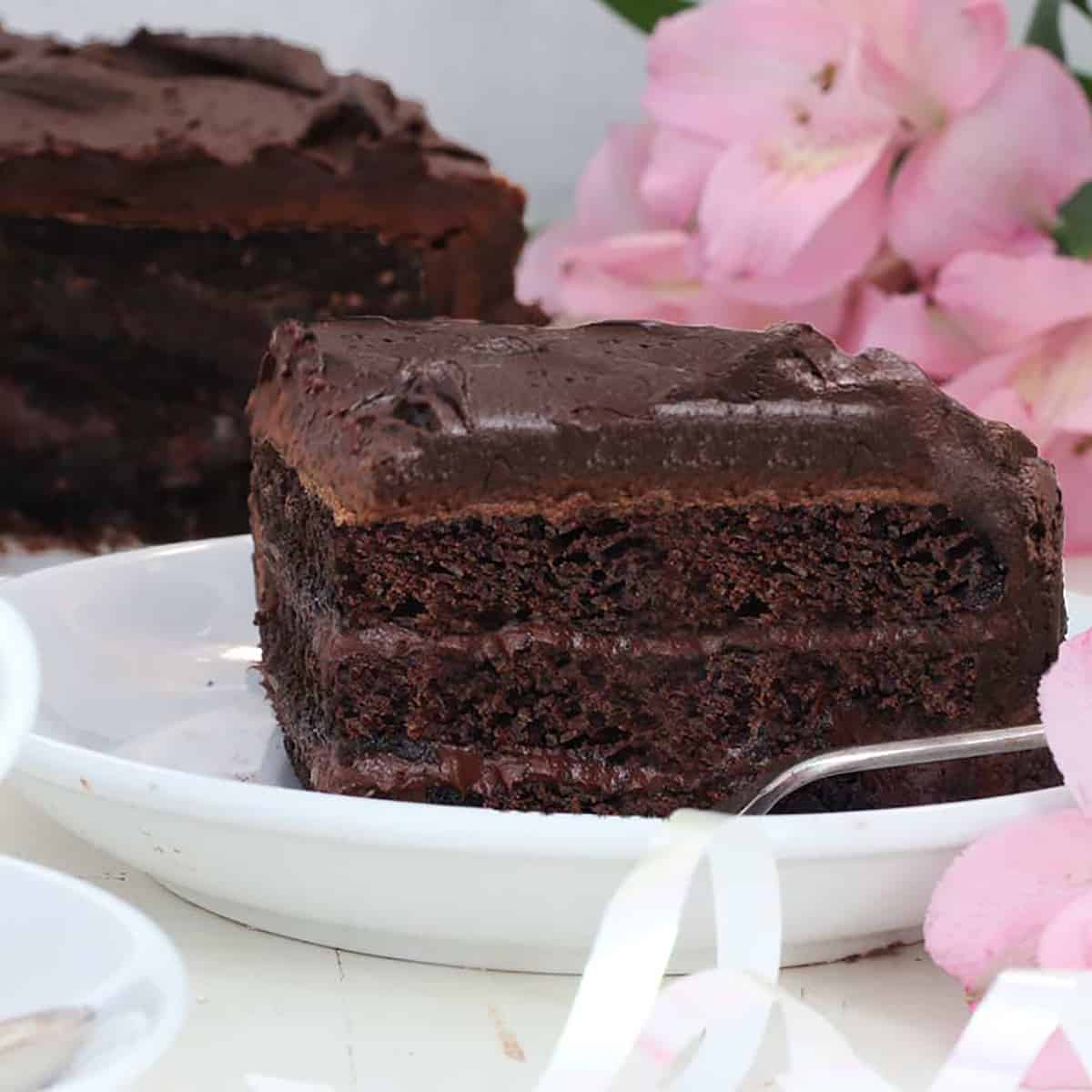 slice of chocolate cake with three layers and a pink flower beside it