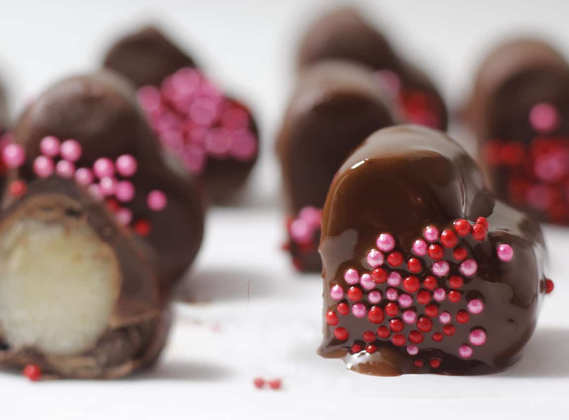 Marzipan frozen hearts dipped in melted chocolate and sprinkled with pink and red sprinkles.