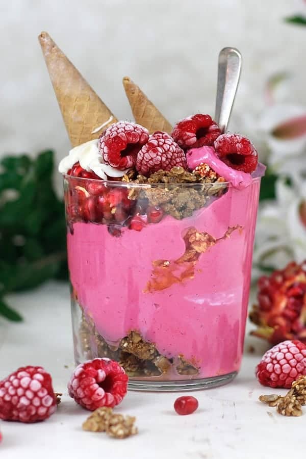 Pink smoothie in a glass with layers of granola and upside down ice cream cones stuck into the top.