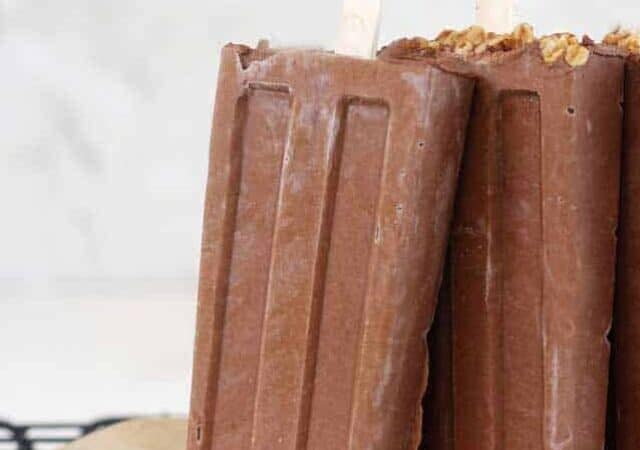 chocolate popsicles standing up on a cooling rack.