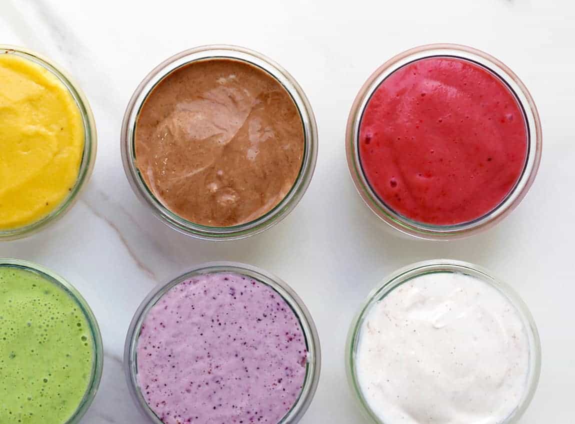 Six rainbow smoothies on a white marble board.