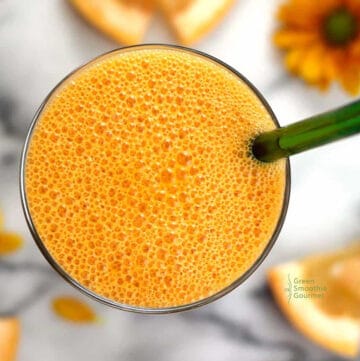 an overhead view of an orange smoothie with green straw