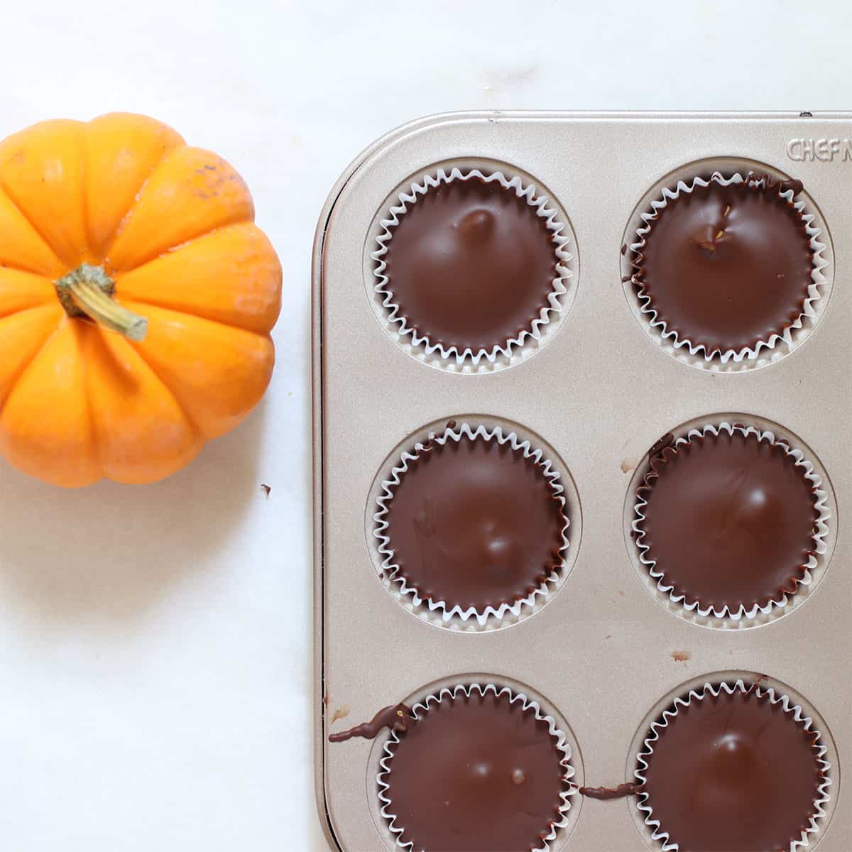 chocolate covered pumpkin fudge cups in a pan with a small pumpkin next to it.