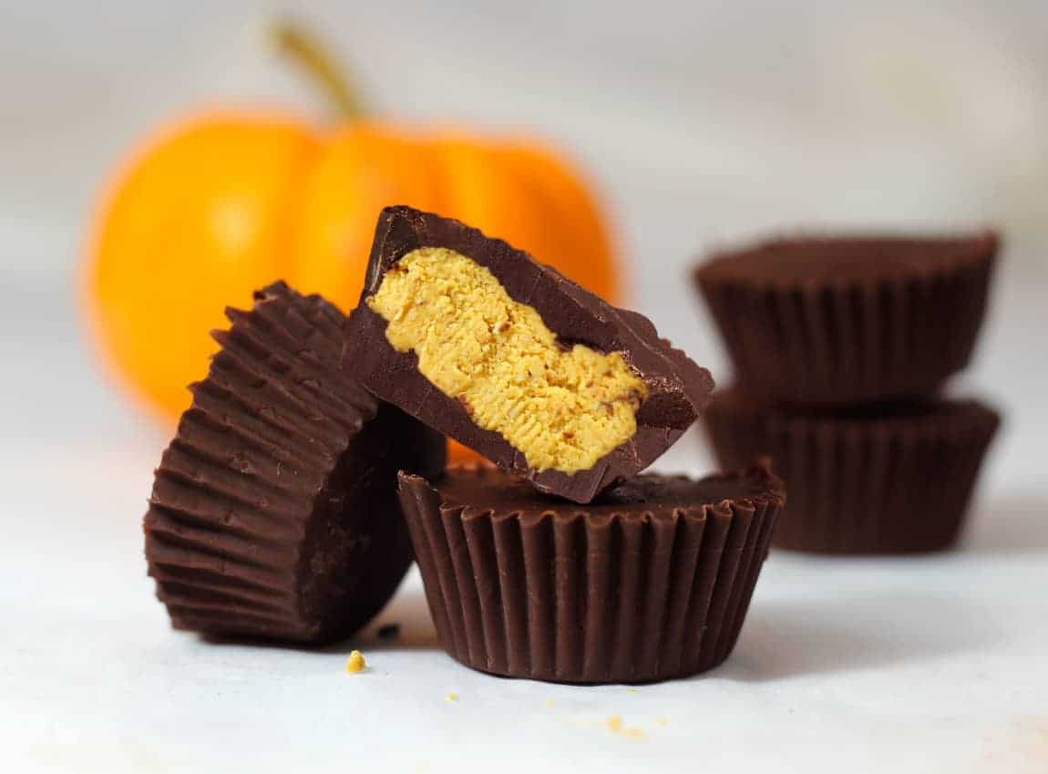 Three chocolate cups filled with pumpkin fudge and with a pumpkin in the background.
