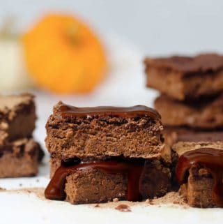 A stack of pumpkin brownies with a dark chocolate drizzle and a pumpkin in the background.