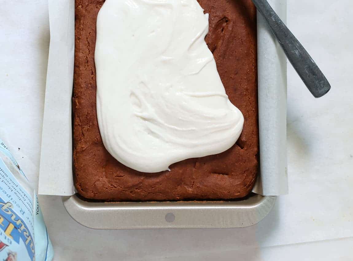Baked pumpkin cake recipe with vegan cream cheese begun to be spread on top of the cake while it is in the pan.