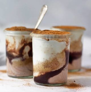 Three jars of healthy homemade mascarpone layered with fudge and cookie crumbs on a white table.