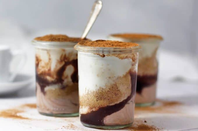Three jars of healthy homemade mascarpone layered with fudge and cookie crumbs on a white table.