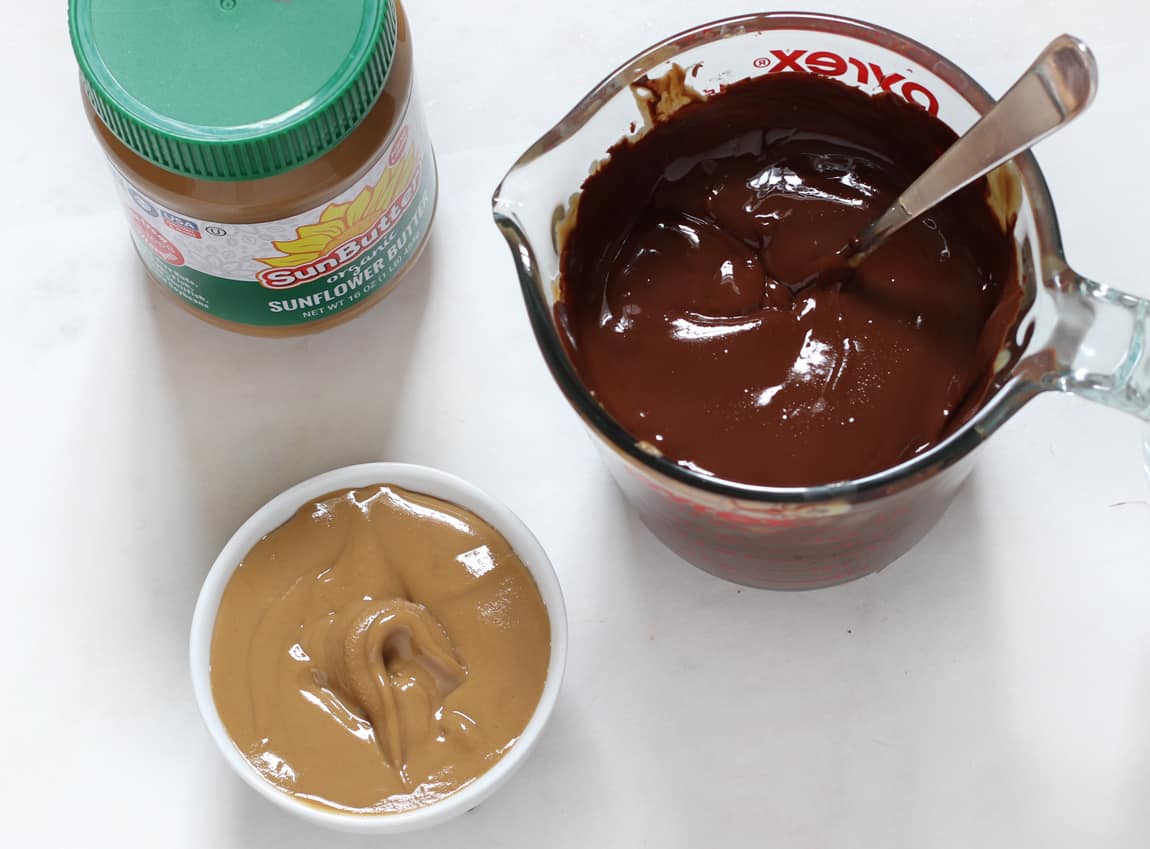 Sunflower seed butter jar with a cup full of melted chocolate and a bowl of sunflower seed butter.