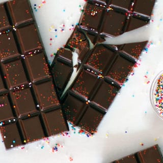 Two homemade chocolate bars on a marble board, broken and with sprinkles.
