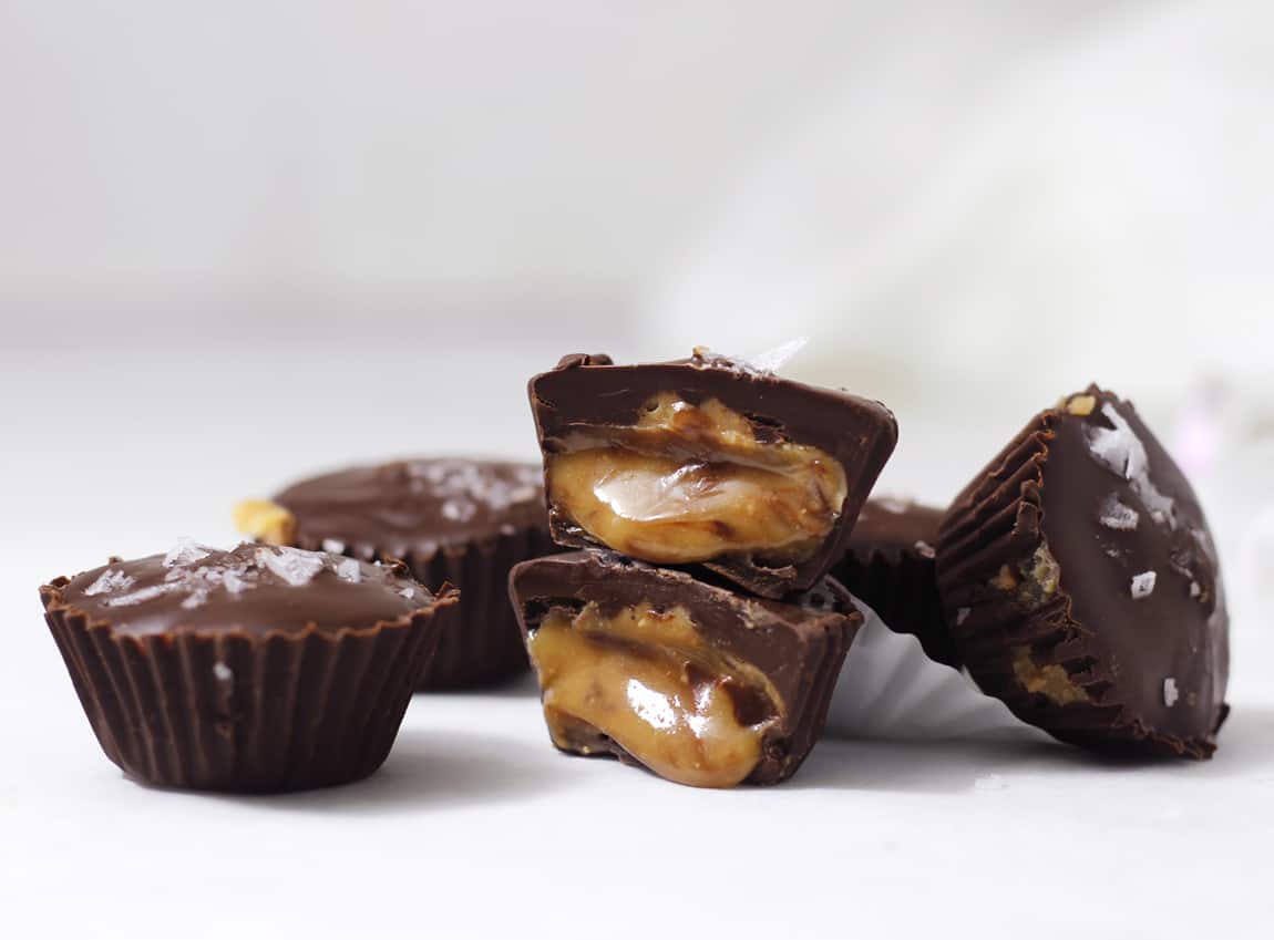 Tower of homemade peanut butter cups with both cut open and spilling out golden creamy peanut butter.