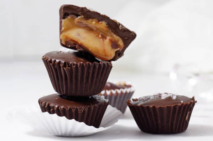 Tower of homemade peanut butter cups with the top one cut open and spilling out golden creamy peanut butter.