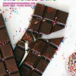 Two homemade chocolate bars on a marble board, broken and with sprinkles.
