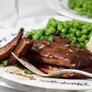 Grilled portobello mushroom steaks, juicy and sliced on a dish with peas and cauliflower mashed potatoes and a water glass to the left.