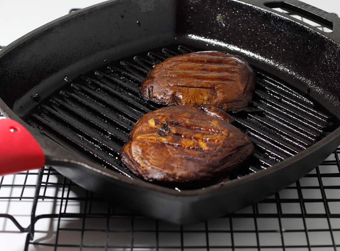 Two grilled portobello caps marinated and juicy in a black grill pan.