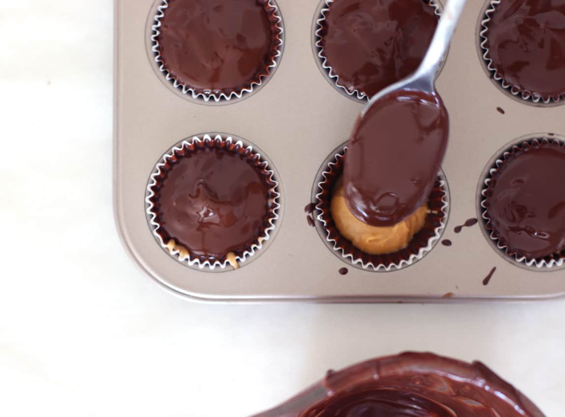 Homemade peanut butter cups being topped with chocolate in pan.