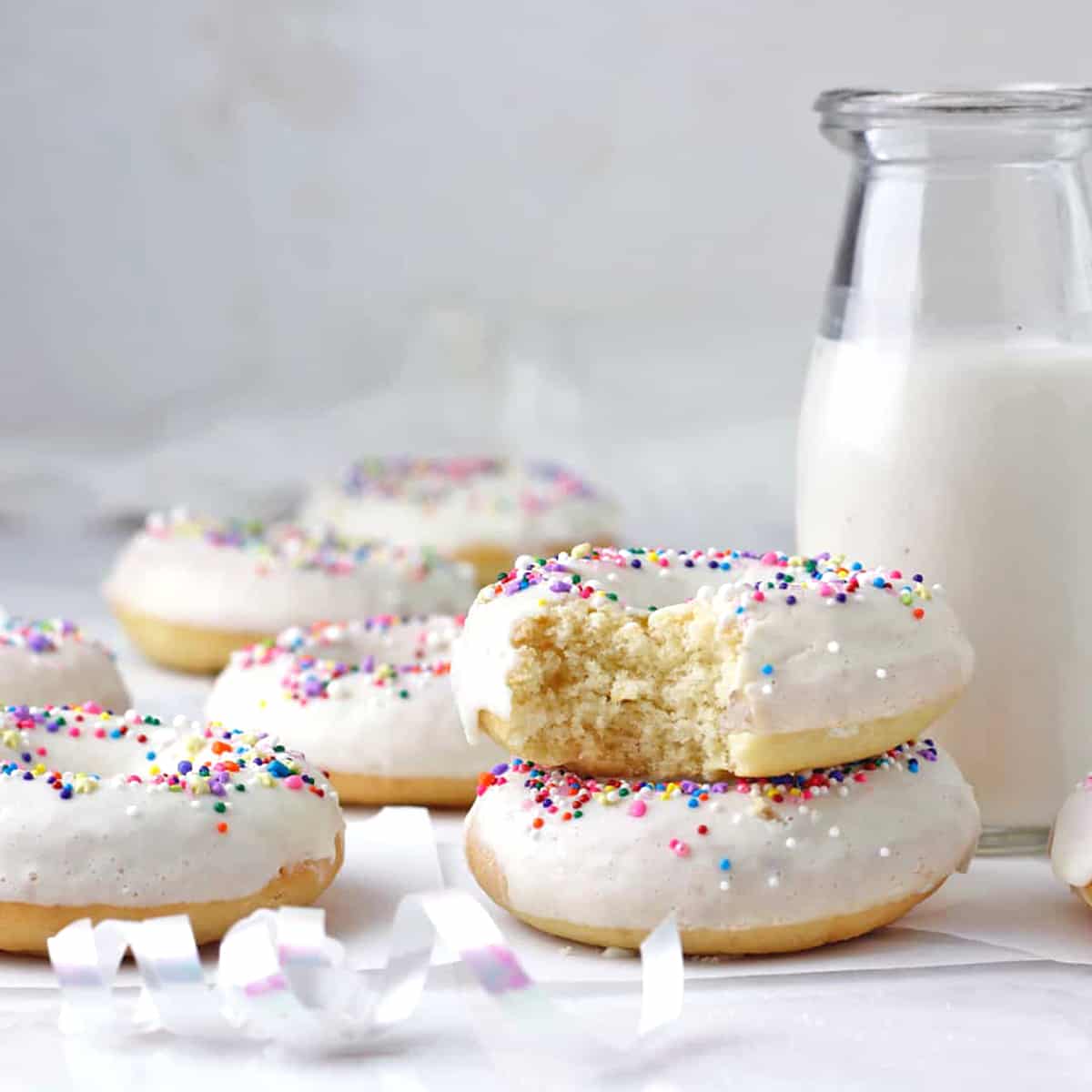 a stack of sprinkle donuts with a bite and milk bottle behind