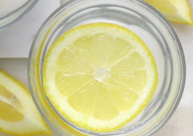 An iced glass of cold lemon water on a marble board.