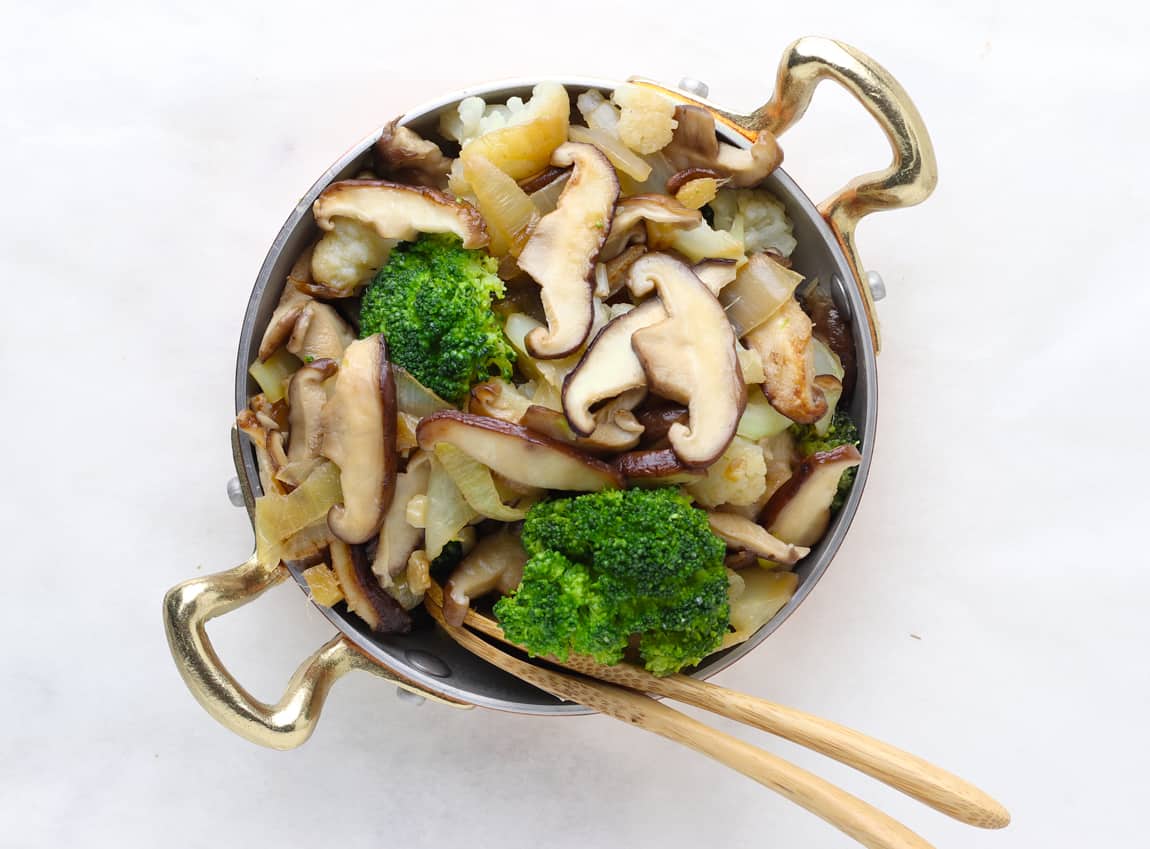 Stir fry mushrooms and broccoli and cauliflower in a brass pan..