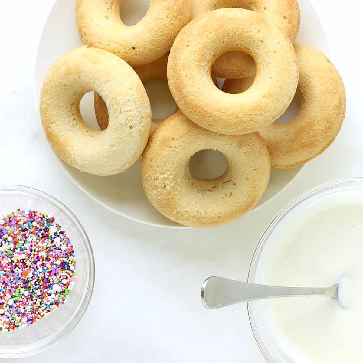 vanilla baked donuts in a dish with a bowl of sprinkles.