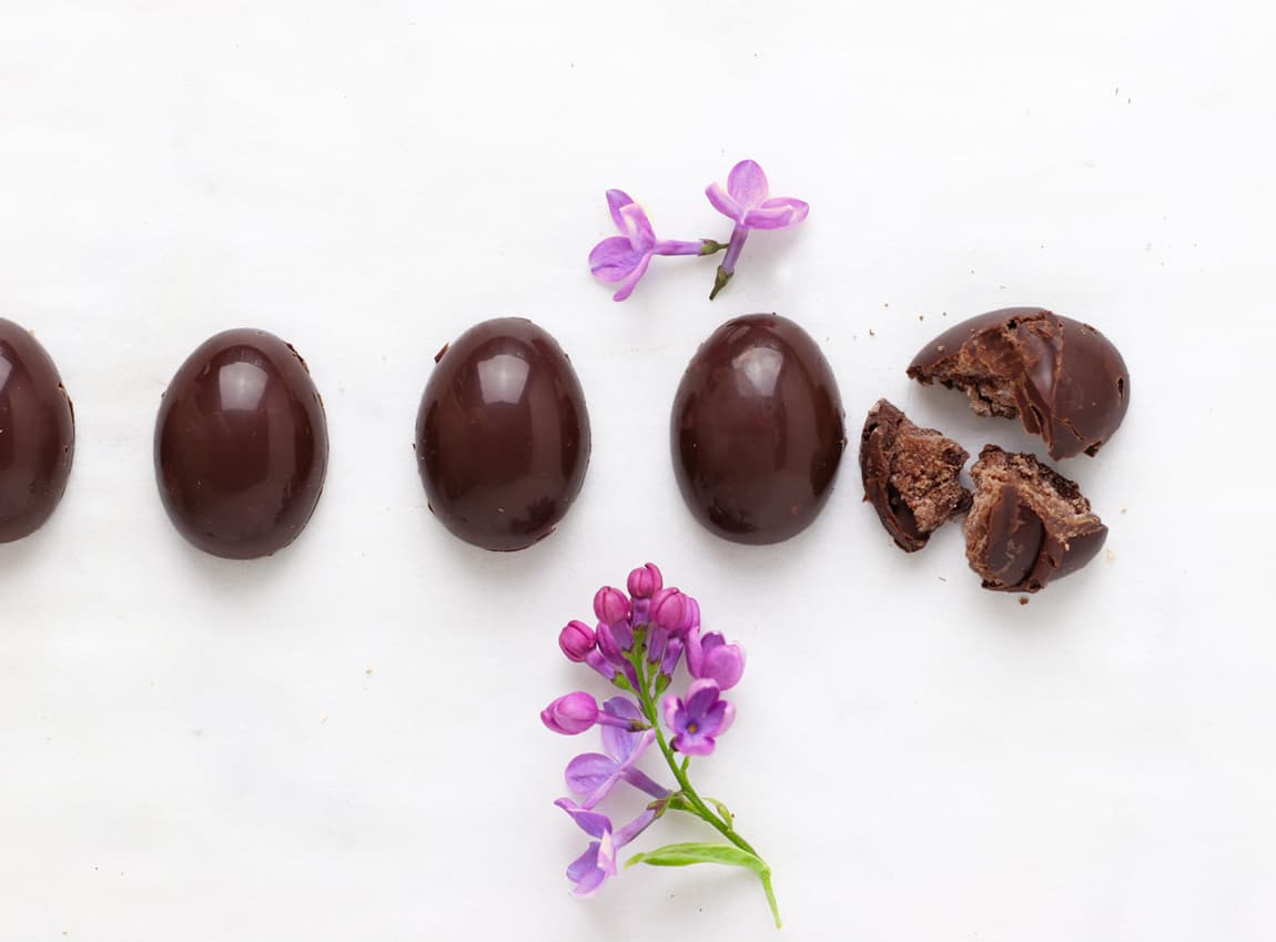 A row of fudge filled eggs on a table with a purple flower bud and one egg is broken.