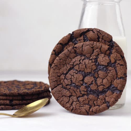 Flourless chocolate cookies stacked next to a bottle of milk.