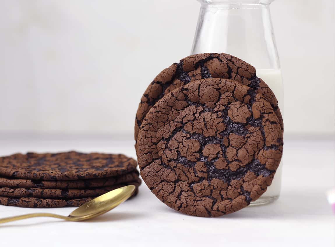 Flourless chocolate cookies stacked next to a bottle of milk.