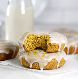 Glazed Pumpkin Baked Donuts with a bite taken out and a jug of milk in background.