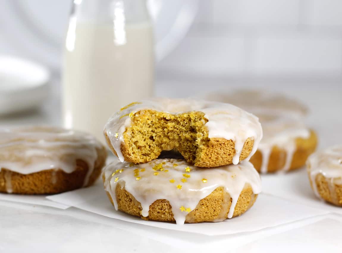 Glazed Baked Pumpkin Donuts with a bite taken out and a jug of milk in background.