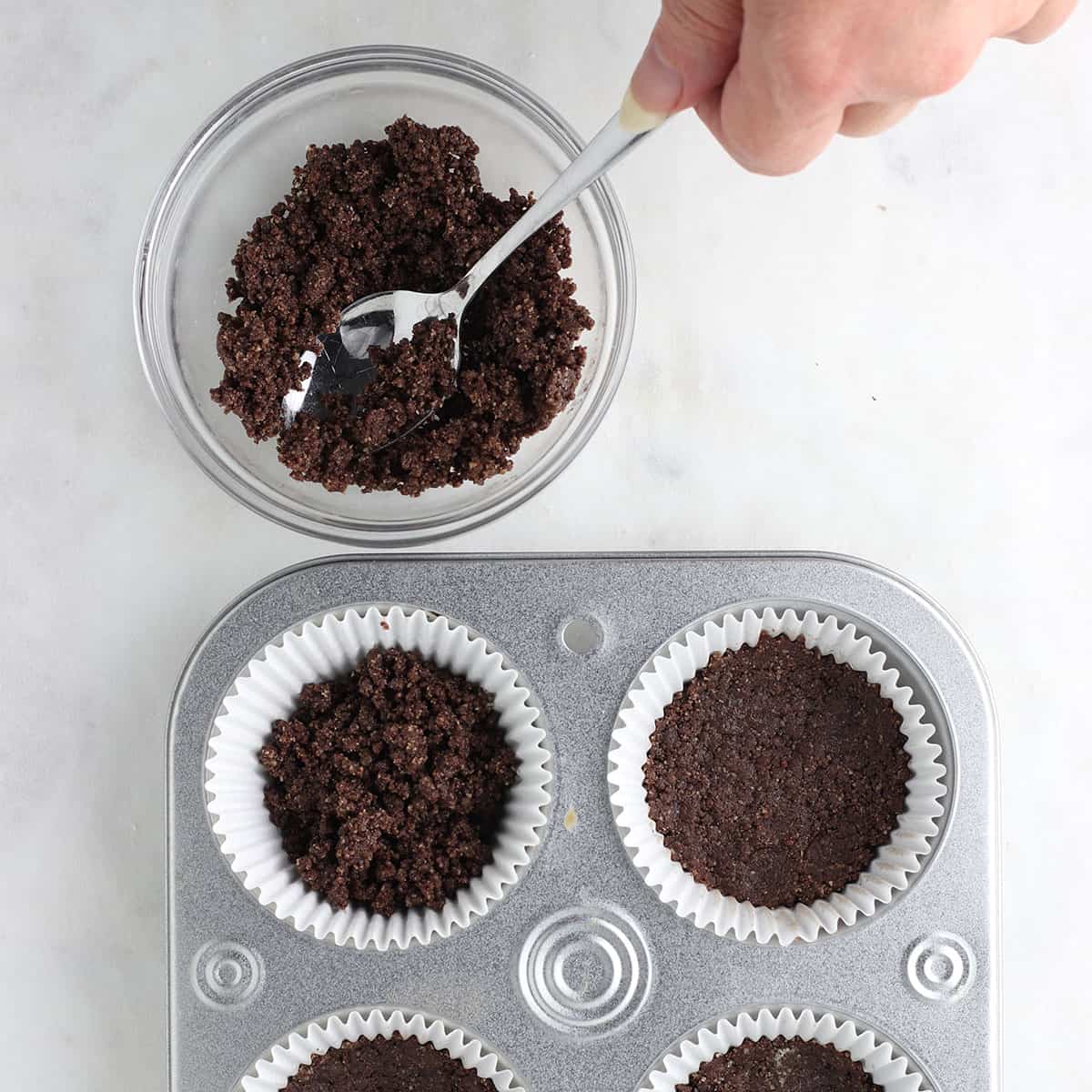adding cookie crust to cupcake pan with spoon.