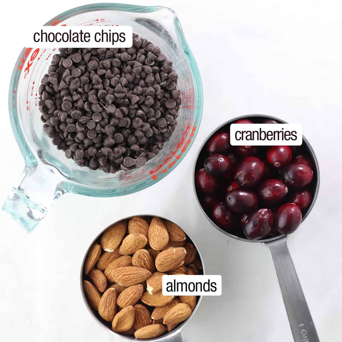 overhead of cranberries, chocolate chips and almonds in cups